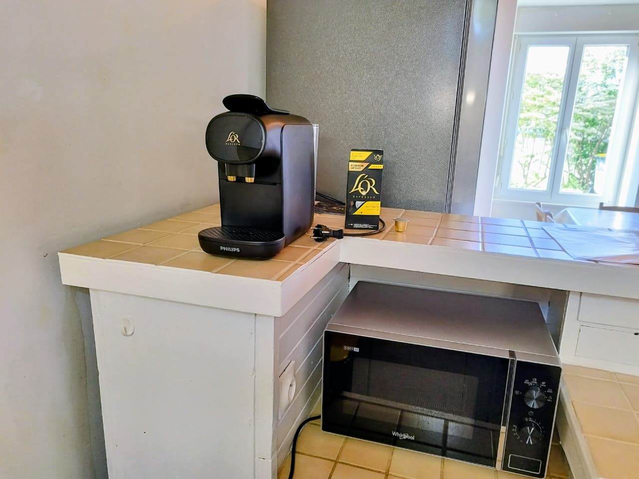 Een compacte kitchenette met een koffiezetapparaat, een magnetron en een doos koffiecups.