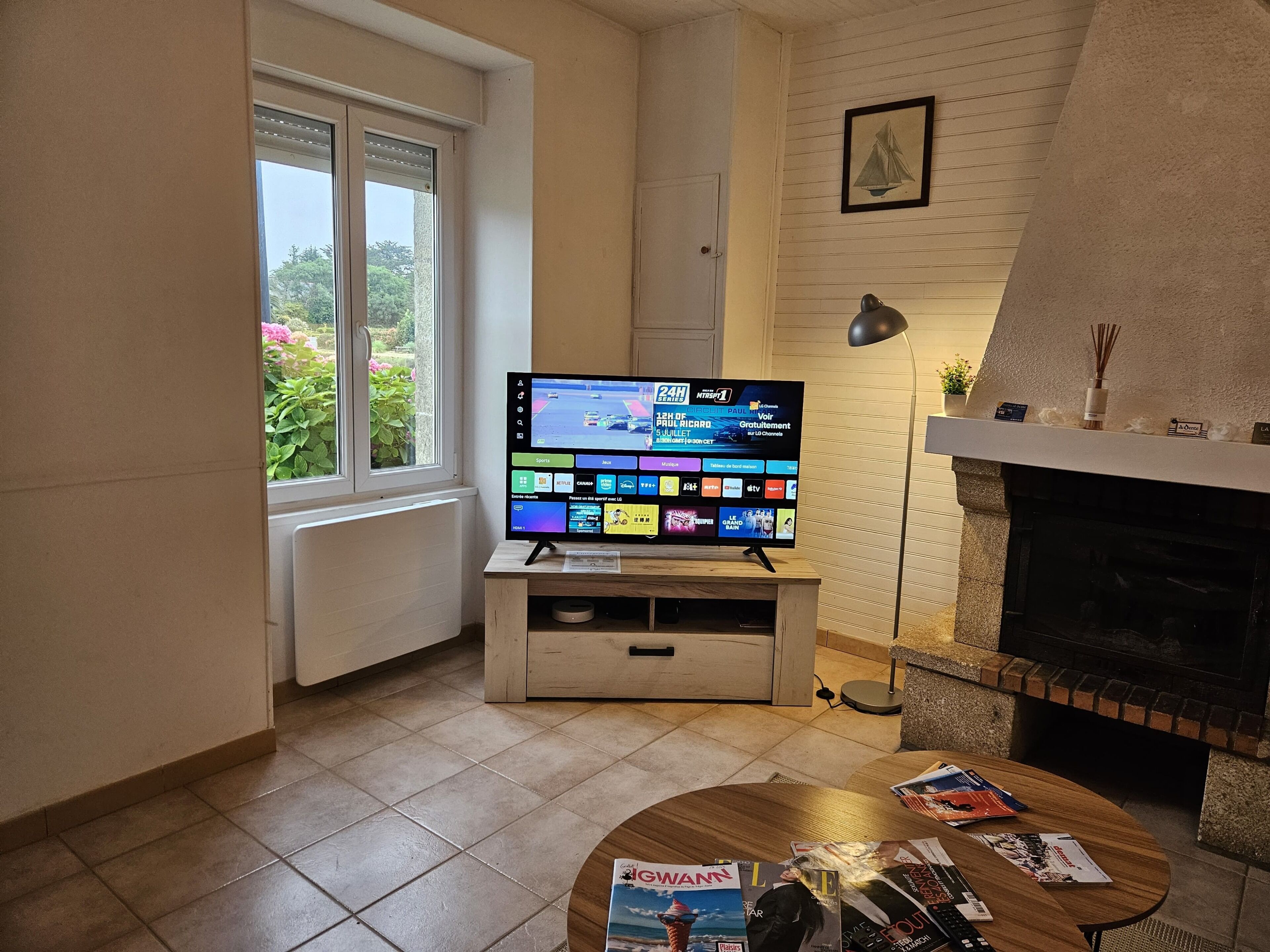 Una sala de estar con televisor de pantalla plana sobre un mueble de madera, chimenea y ventana con vista a follaje.