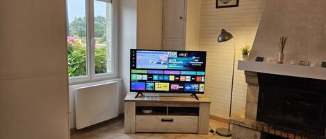 Una sala de estar con televisor de pantalla plana sobre un mueble de madera, chimenea y ventana con vista a follaje.