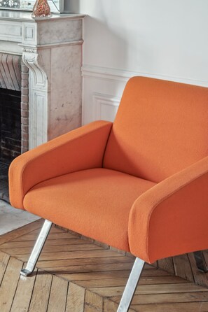 Ein moderner, orangefarbener Sessel mit Metallbeinen, platziert auf einem Holzbodenparkett.