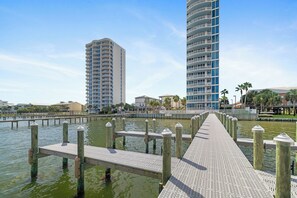 Eine Uferpromenade mit einem hölzernen Steg, der zu einem Yachthafen führt, gesäumt von modernen Hochhäusern.