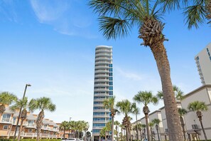 Un hotel alt i modern amb múltiples balcons i una palmera al primer pla.