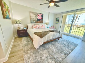 A bedroom with a bed, bedside tables, a ceiling fan, and a view of the outdoors. - First Floor | Priv Beach | Pool & Pickleball (Cocoa Beach)