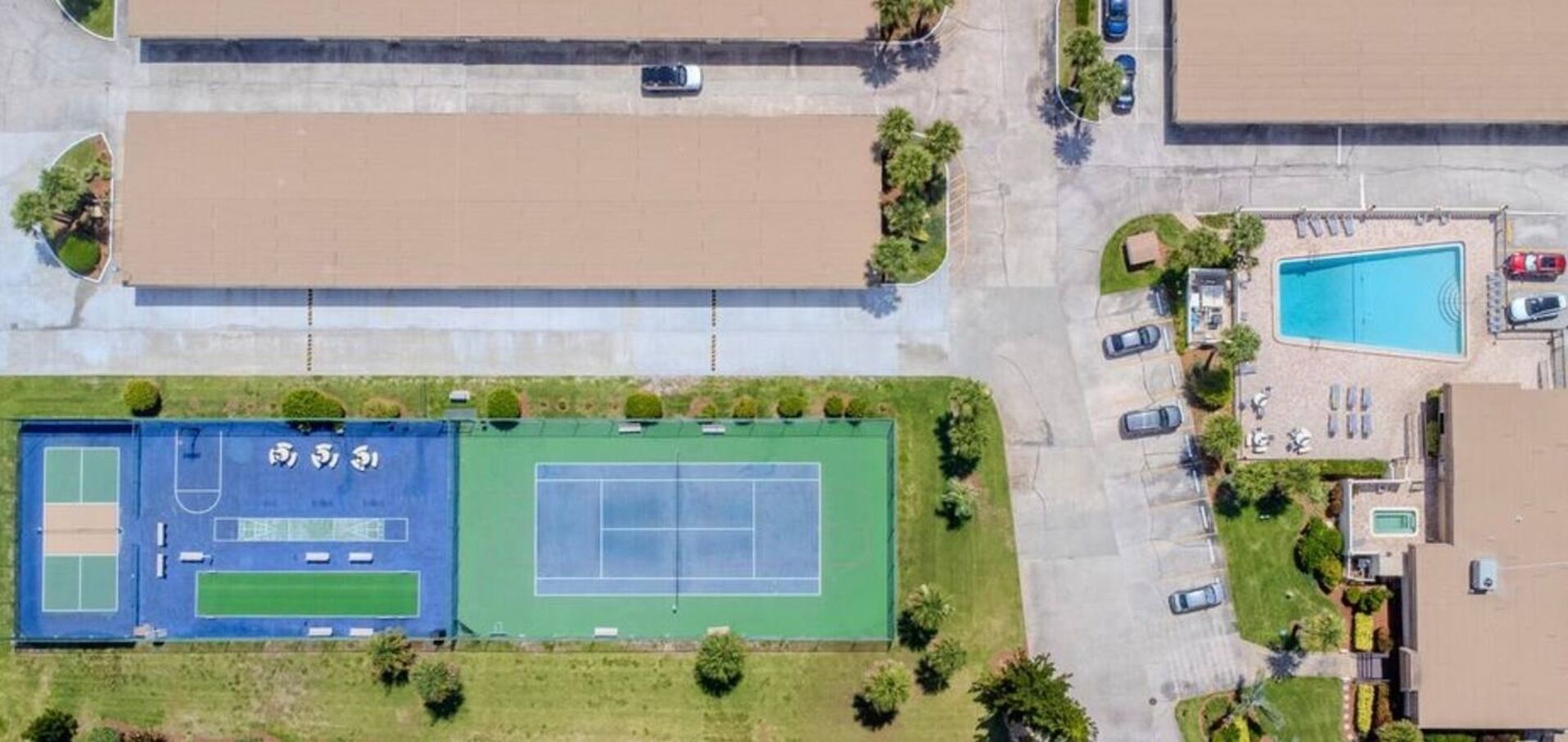 An aerial view of a residential area with a tennis court, parking spaces, and a swimming pool.