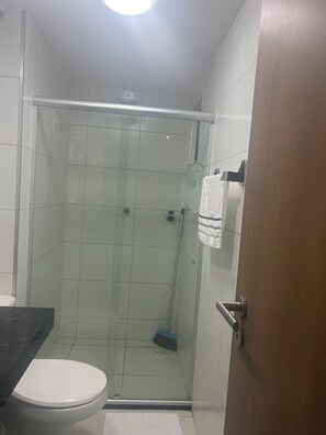 Kylpyhuoneessa on lasiseinällä varustettu suihku, valkoinen wc-istuin ja puuovi.