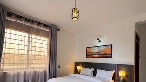 Un dormitorio con una cama grande, dos mesitas de noche con lámparas, un cuadro en la pared y una ventana con cortinas.
