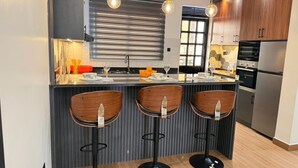 Cocina moderna con una isla central, taburetes de bar, electrodomésticos de acero inoxidable e iluminación colgante.