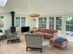 A spacious living room with a fireplace, comfortable seating, and large windows. - Wooden house close to the sea in Hornbæk (Hornbæk)