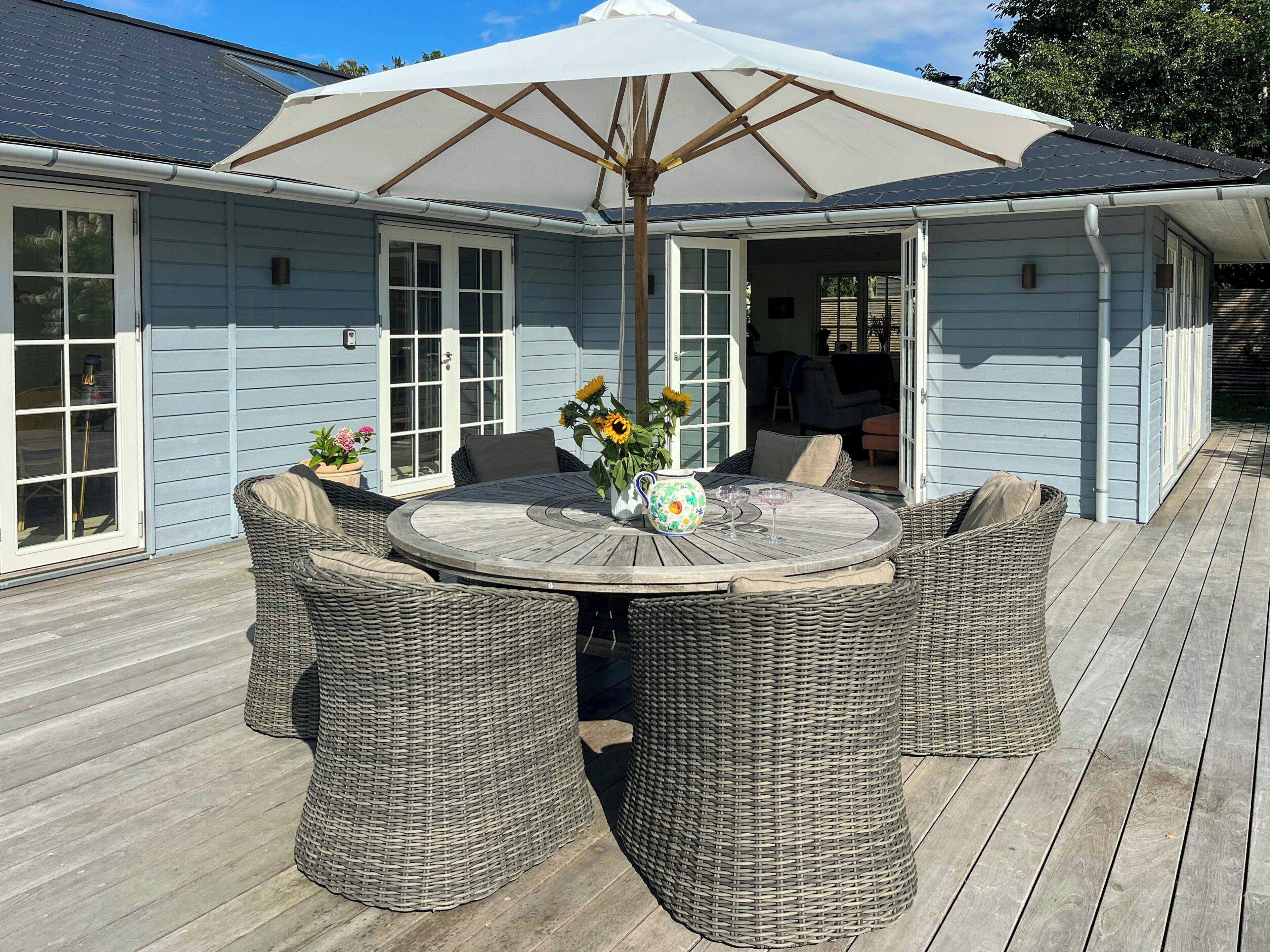 A covered outdoor seating area with wicker furniture, a table, and a large umbrella.