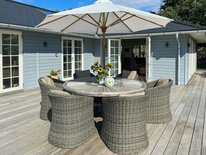 A covered outdoor seating area with wicker furniture, a table, and a large umbrella. - Wooden house close to the sea in Hornbæk (Hornbæk)