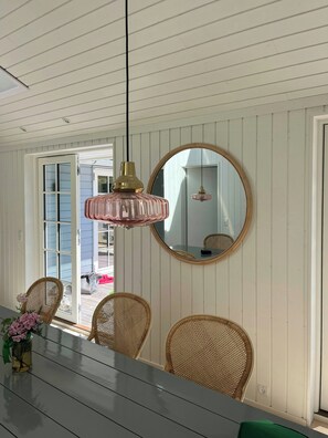 A dining area with a table, chairs, a hanging pendant light, and a round mirror on the wall. - Wooden house close to the sea in Hornbæk (Hornbæk)