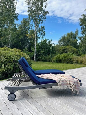 Ein Liegestuhl mit Decke auf einer Holzterrasse.