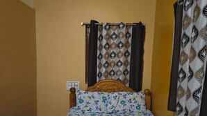 A single bed with a floral bedspread, a wooden headboard, and a window with curtains. - Gorgeous 6-bedroom house with AC in charming Sanapur (Sanapur)