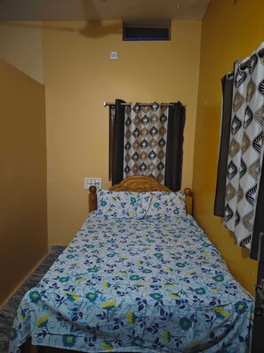 A single bed with a floral bedspread, a wooden headboard, and a window with curtains. - Gorgeous 6-bedroom house with AC in charming Sanapur (Sanapur)