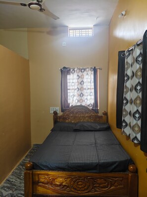 A single bed with a wooden headboard, a ceiling fan, a window with curtains, and a wall-mounted light fixture. - Gorgeous 6-bedroom house with AC in charming Sanapur (Sanapur)