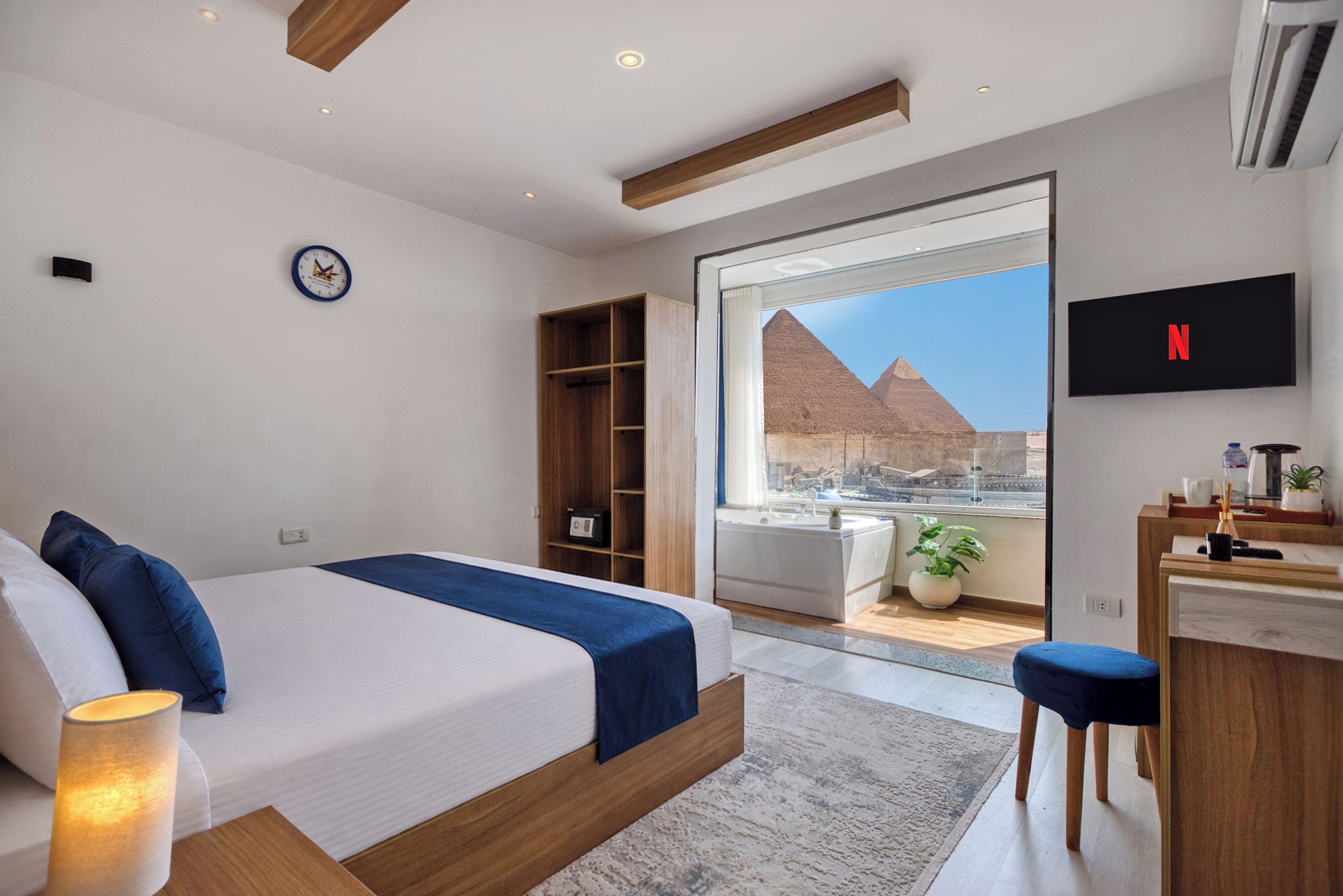 Ein modernes Schlafzimmer mit Bett, Fernseher, Schreibtisch und Blick auf eine Pyramide.