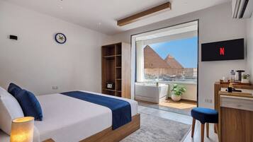 Ein modernes Schlafzimmer mit Bett, Fernseher, Schreibtisch und Blick auf eine Pyramide.