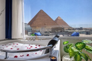 A bathtub with rose petals, a potted plant, and a view of the pyramids. - My Pyramids View Inn Jacuzzi & Rooftop (Giza)