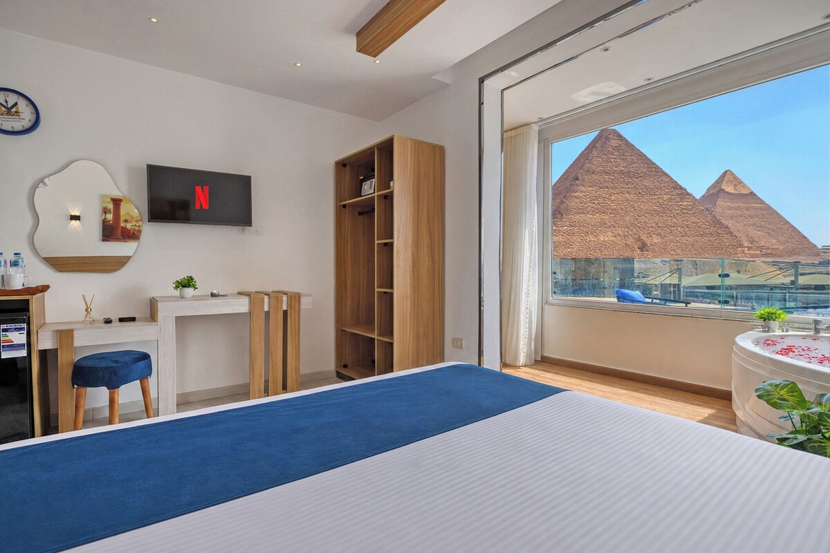 A modern hotel room with a large window, a bed, a desk, a wardrobe, and a TV.