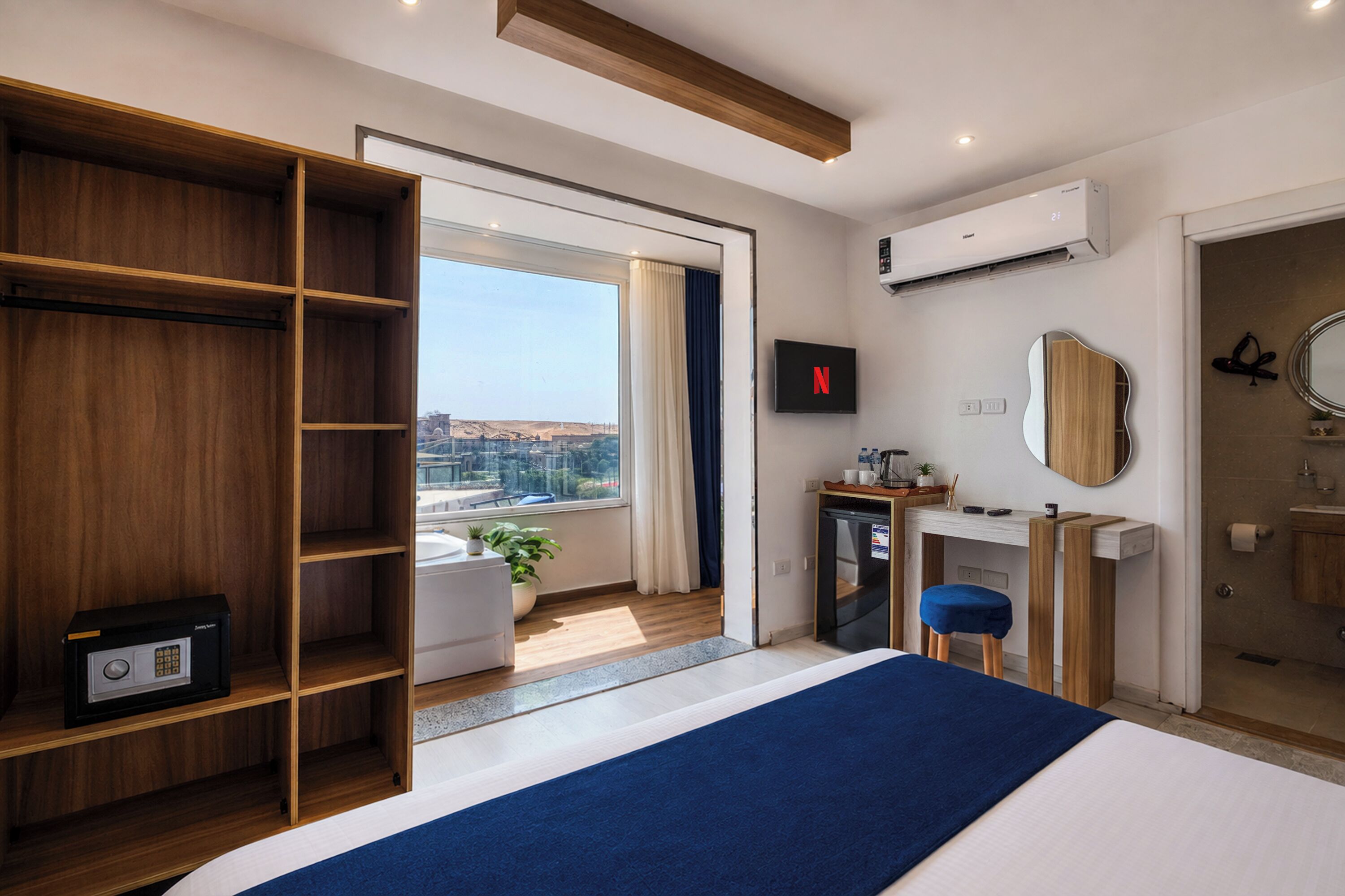 A hotel room with a large bed, a wardrobe, a desk with a computer, a TV, and a view of the city.