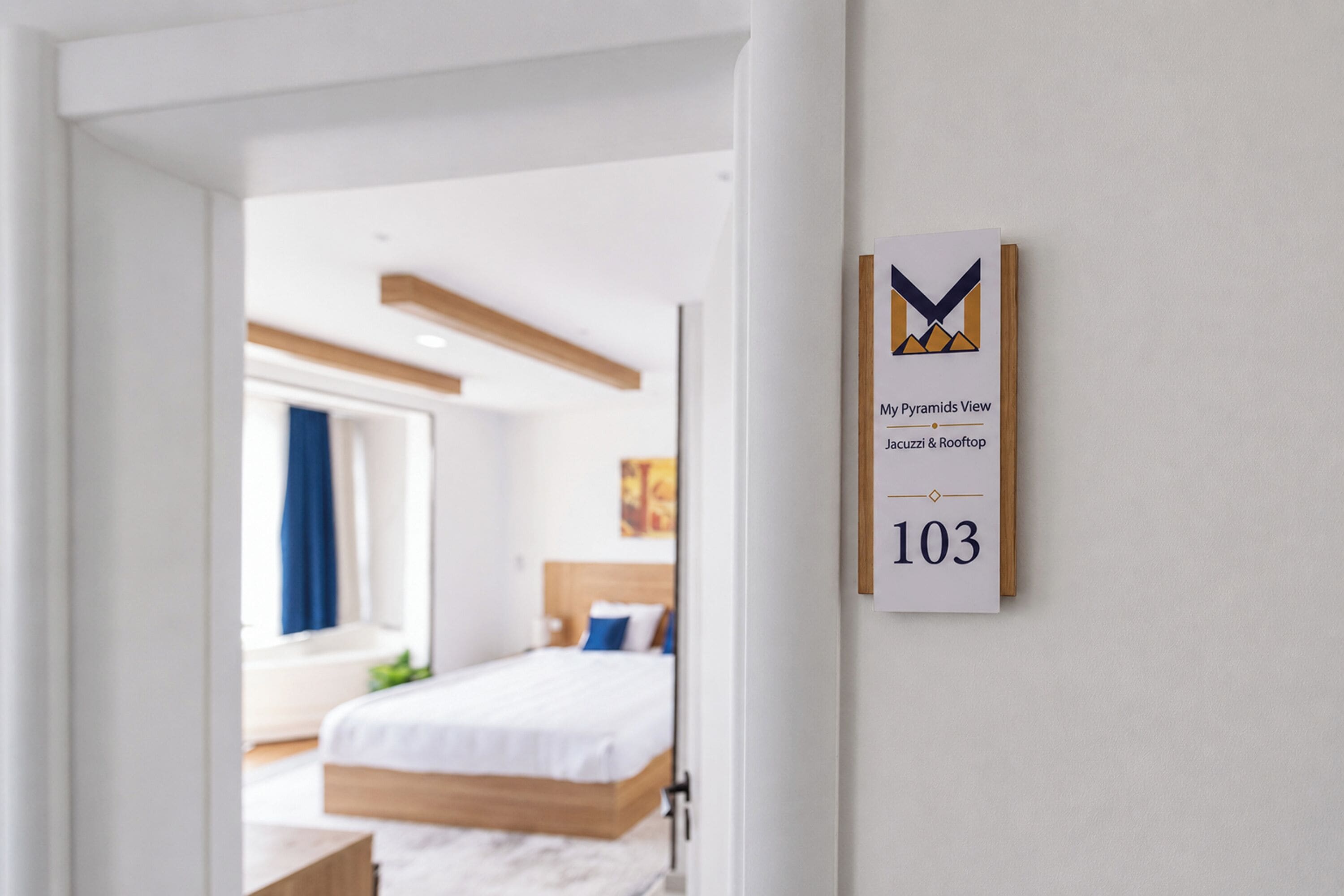 Habitación de hotel con una cama, una ventana con cortinas y un cartel en la pared que indica el número de habitación 103.