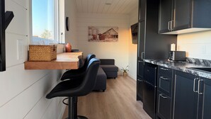 A modern kitchen with a built-in bar area, dark cabinets, and a large window.