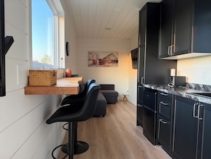 A modern kitchen with a built-in bar area, dark cabinets, and a large window.