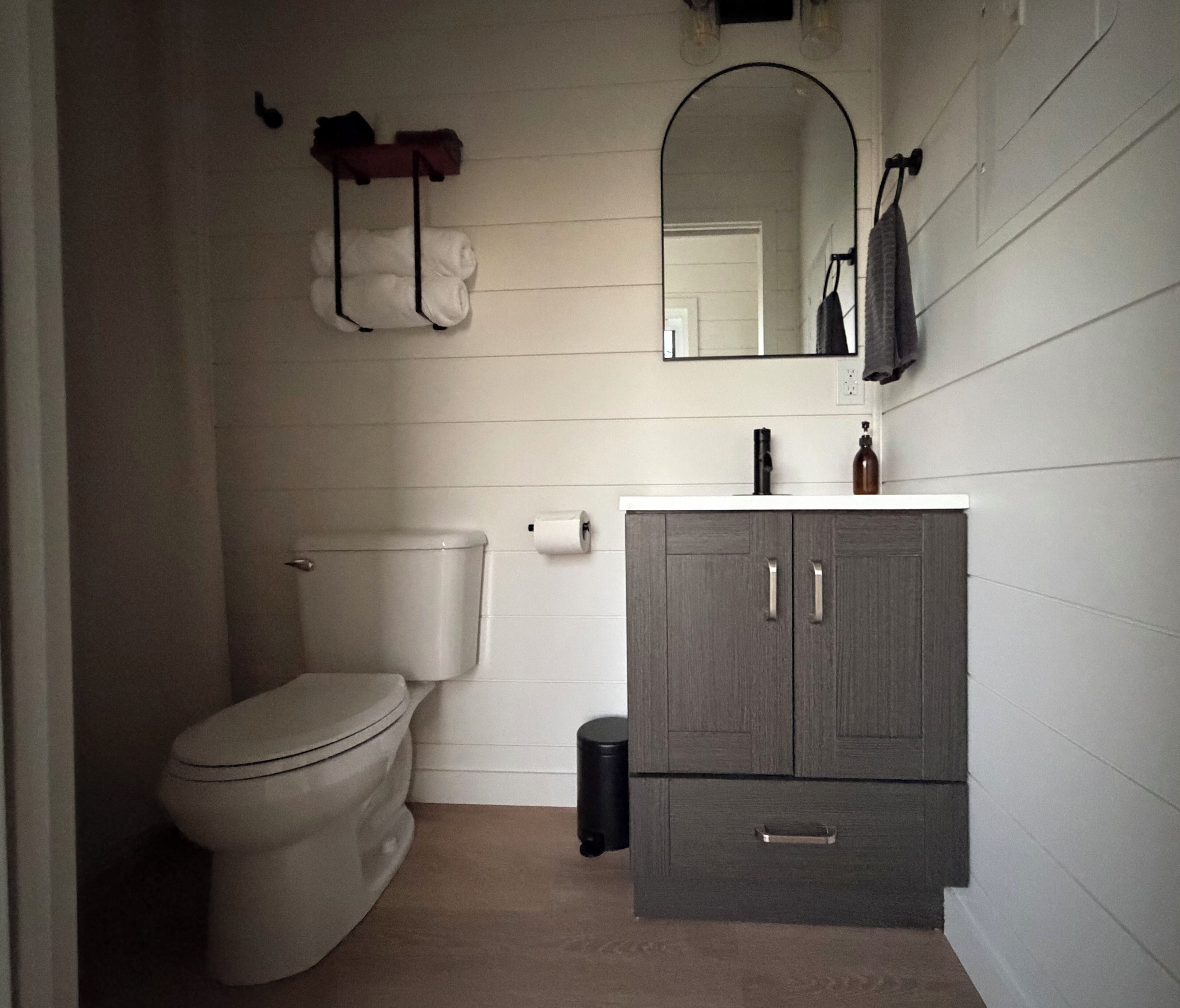 Un baño con inodoro, lavamanos con espejo y un armario.