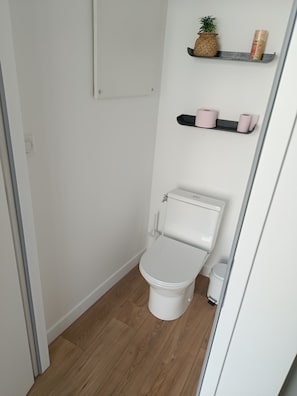 Ein kleines, sauberes Badezimmer mit einer weißen Toilette, Holzboden und Ablage für Toilettenartikel.