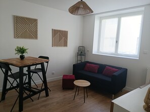 Ein stilvolles Wohnzimmer mit Esstisch, Stühlen, einer Couch, einem kleinen runden Tisch und einer Topfpflanze.