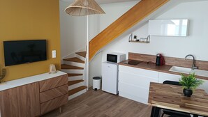 Une cuisine moderne avec un escalier en bois, des meubles blancs, une table à manger agrémentée d’une plante et un téléviseur fixé au mur.