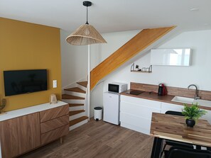 Eine moderne Küche mit einer Holztreppe, weißen Schränken, einem Esstisch mit einer Pflanze und einem an der Wand montierten Fernseher.