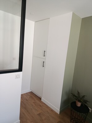 Ein Zimmer mit einem weißen Kleiderschrank, einem kleinen runden Tisch mit einer Pflanze und Holzdielen.