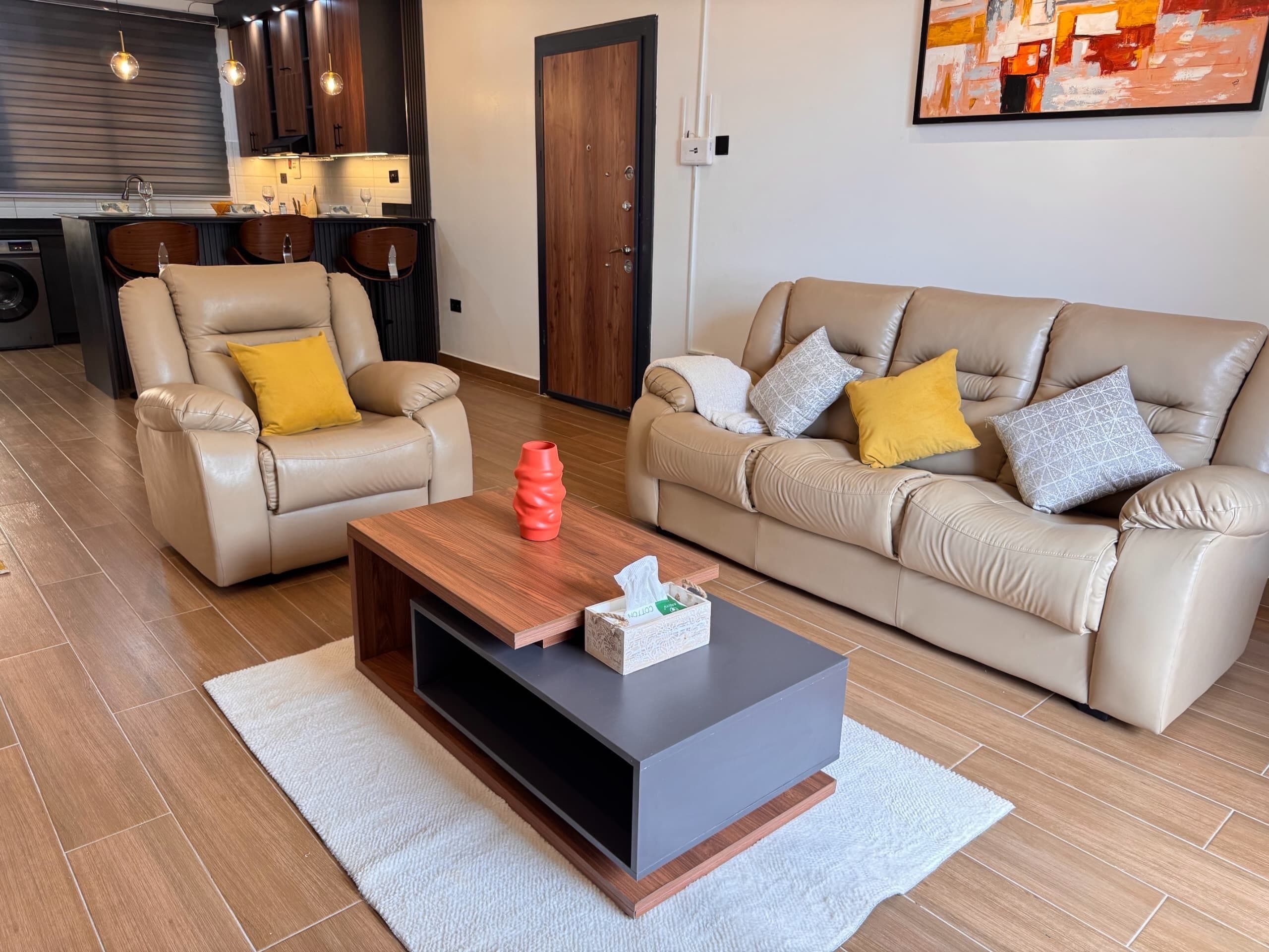 A modern living room with two leather sofas, a wooden coffee table, and a kitchen in the background.