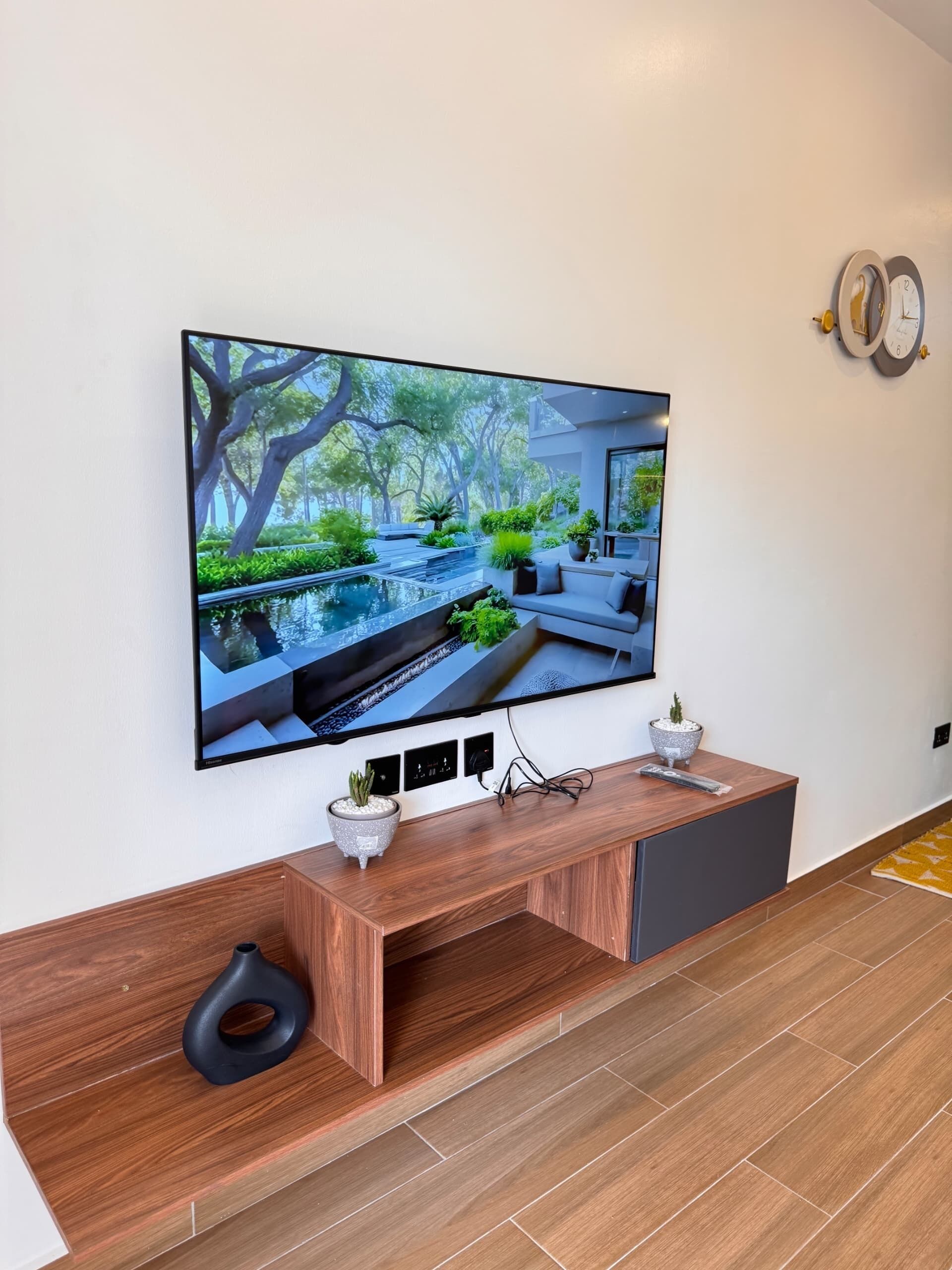 A flat-screen TV mounted on a wall above a wooden console with a potted plant.