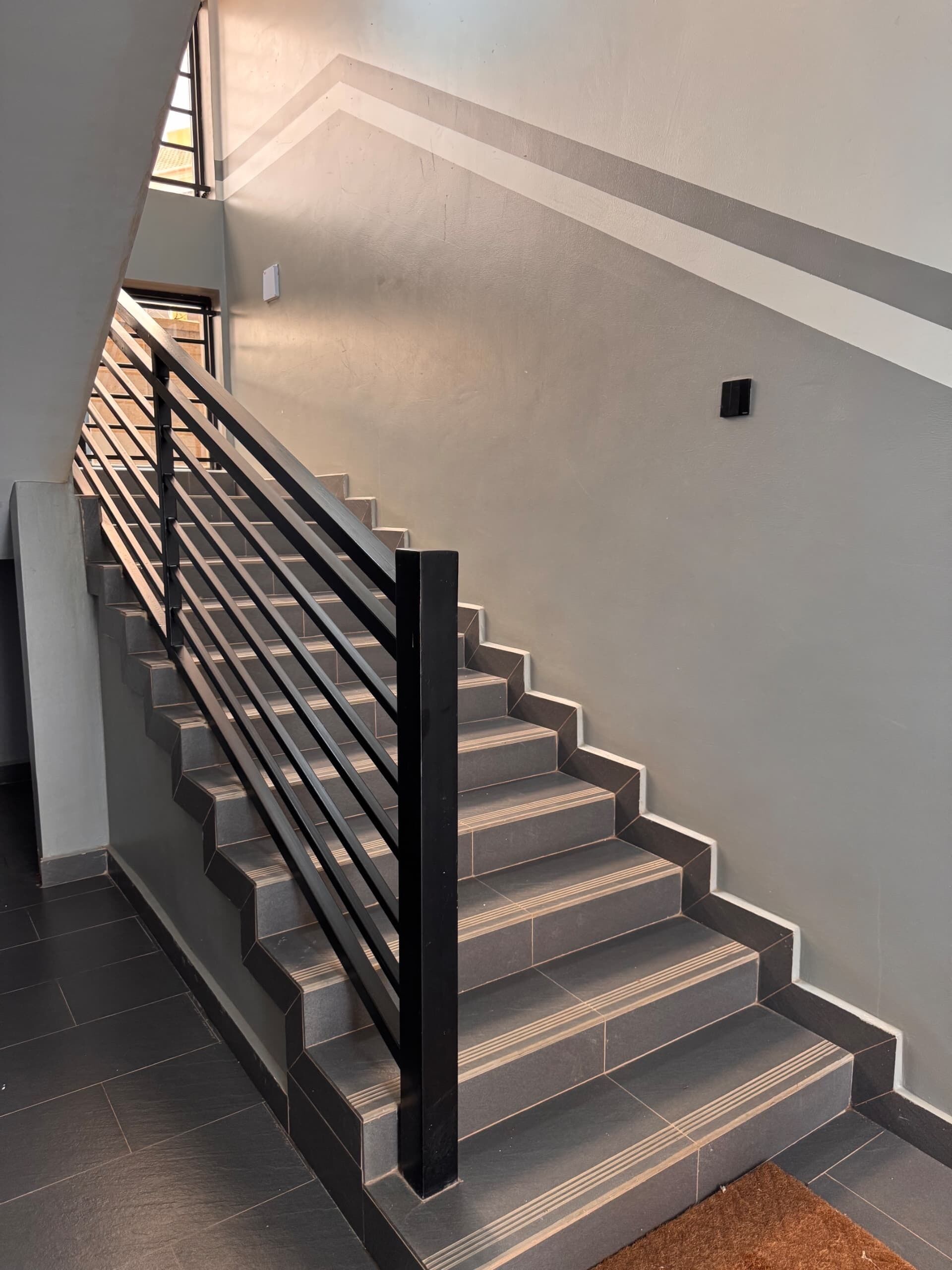 Un escalier avec une rampe métallique et des marches sombres.