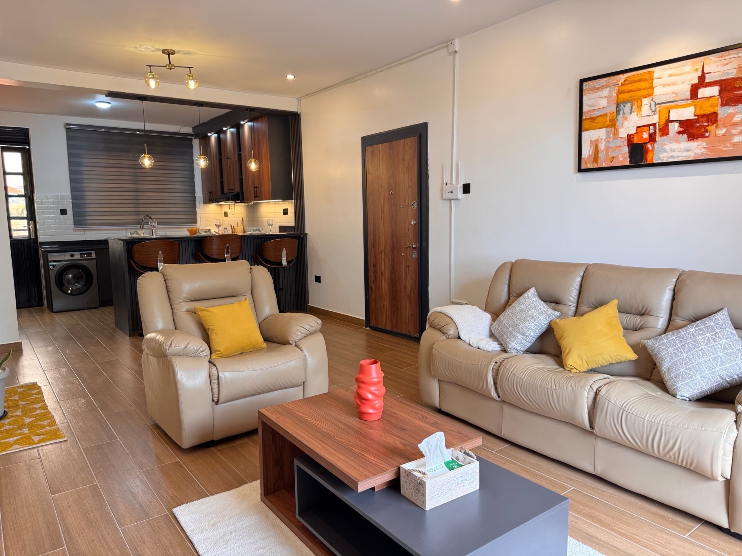 Een moderne woonkamer met een bank, fauteuil, salontafel en een schilderij aan de muur.