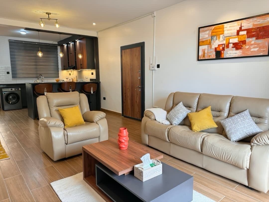 Een moderne woonkamer met twee leren banken, een salontafel en een keuken op de achtergrond.