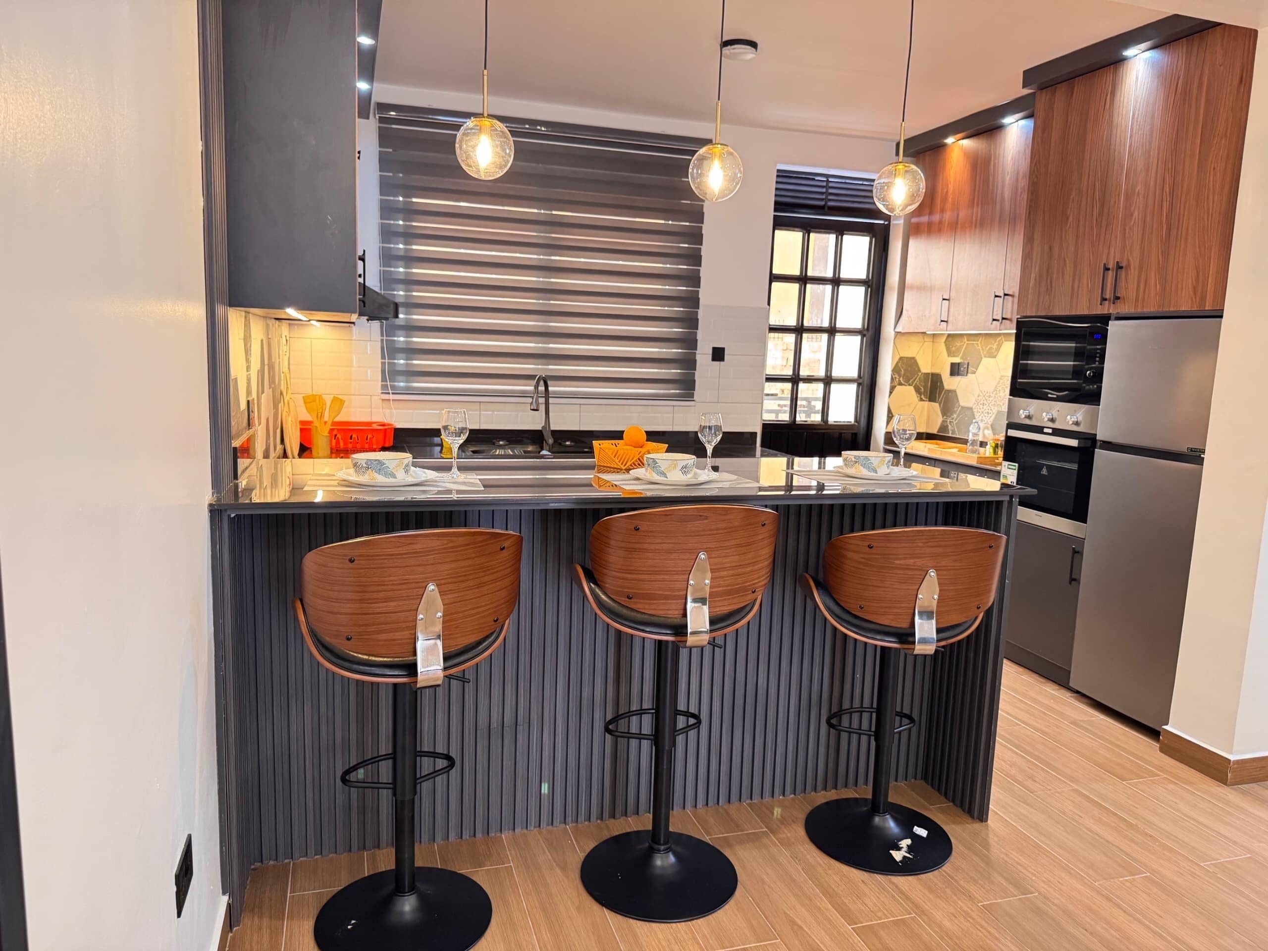 Een moderne keuken met een centraal eiland, barkrukken, een ingebouwde oven en een koelkast.