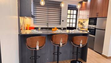 Een moderne keuken met een centraal eiland, barkrukken, een ingebouwde oven en een koelkast.