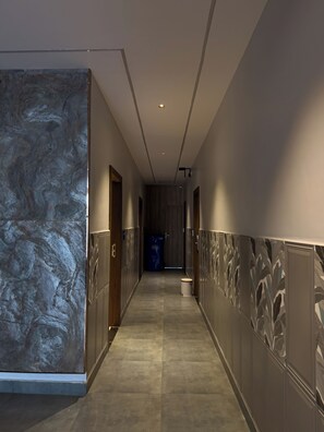 A hallway with a marble wall on one side and a patterned wall on the other, leading to a door at the end.