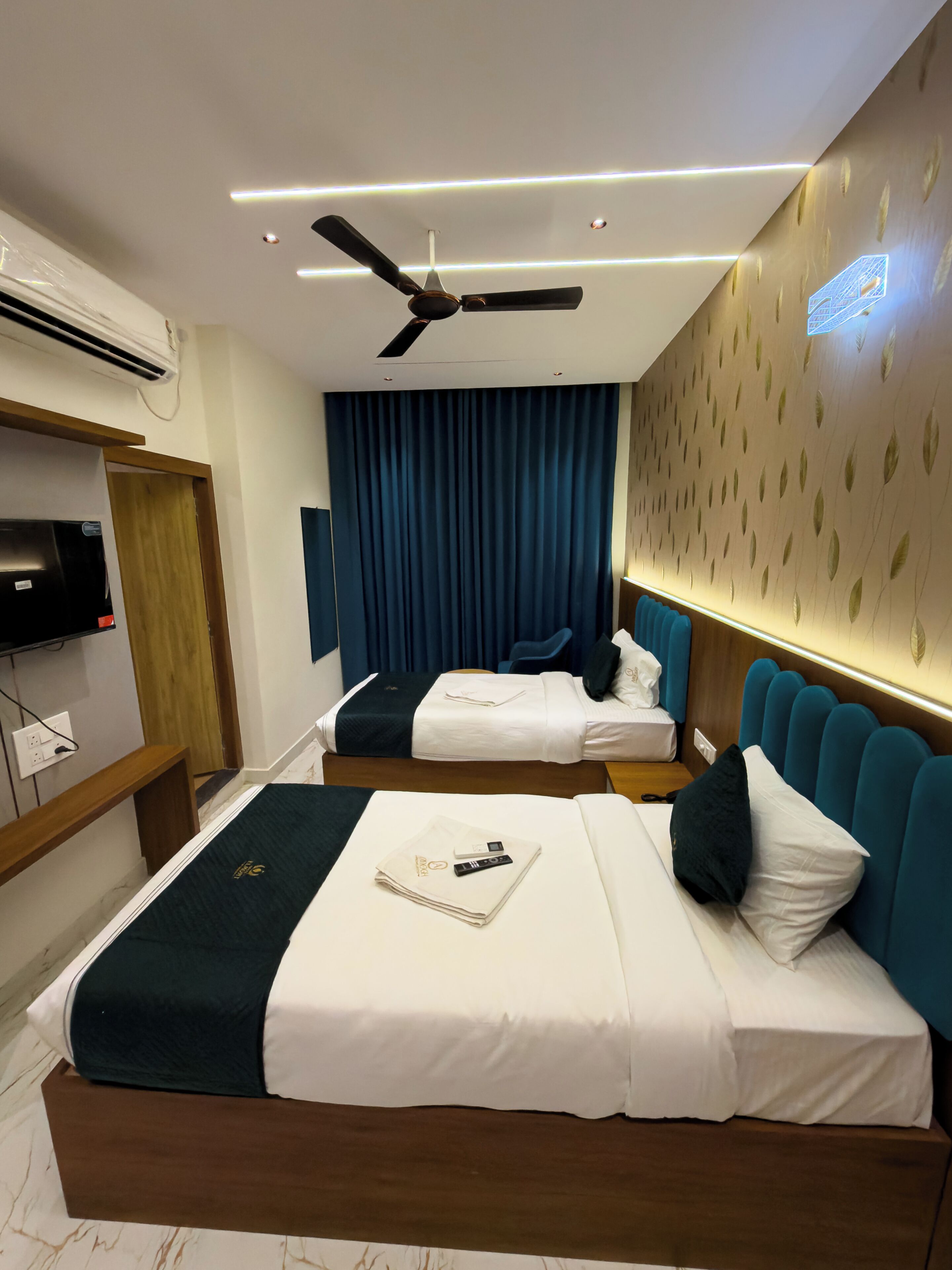 Habitación de hotel con dos camas, ventilador de techo, televisión de pantalla plana y aire acondicionado de pared.