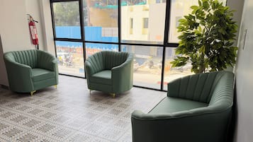 Ein Zimmer mit drei grünen Sesseln, einem gemusterten Boden und einem großen Fenster mit Blick auf eine Baustelle.