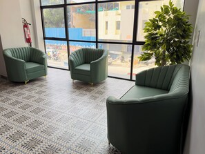 A room with three green armchairs, a patterned floor, and a large window with a view of a construction site.