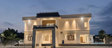 A two-story house with a balcony, a swimming pool, and a well-maintained lawn.