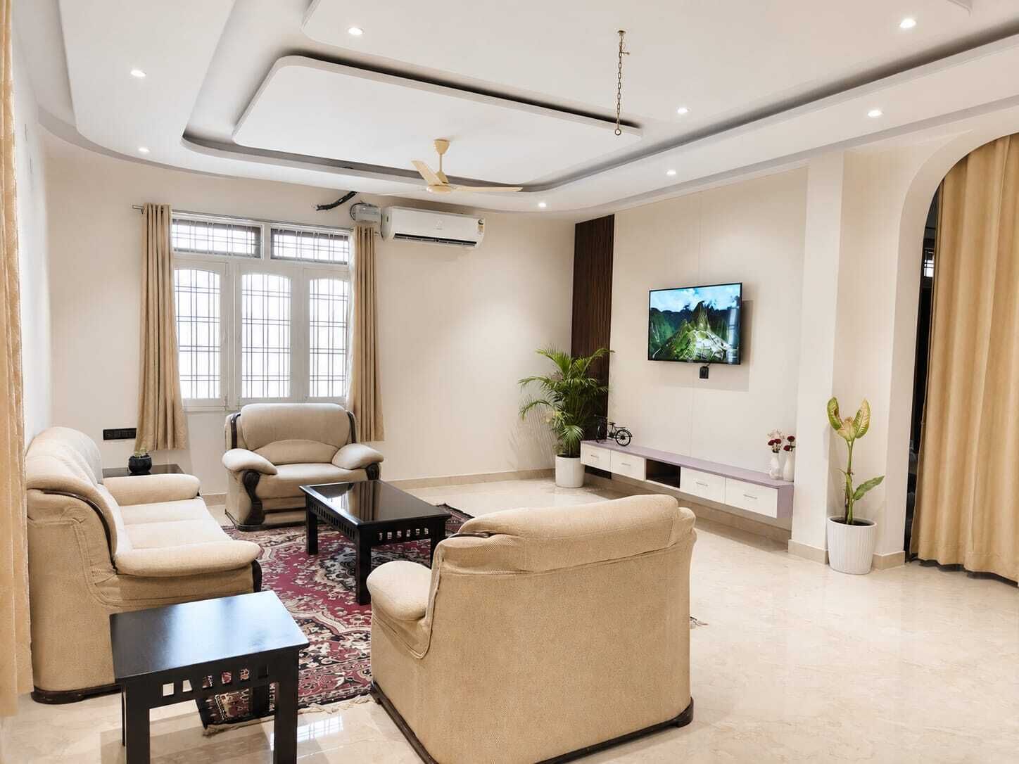 A modern living room with a sofa set, a coffee table, a TV mounted on the wall, and a ceiling fan.