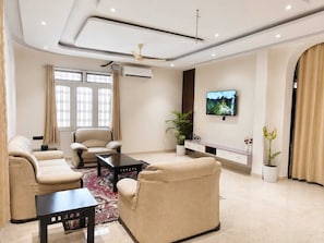 A modern living room with a sofa set, a coffee table, a TV mounted on the wall, and a ceiling fan.