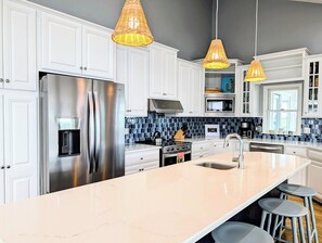 Et moderne køkken med hvide skabe, et rustfrit stål køleskab, en stor ø med barstole og en backsplash i blå fliser.