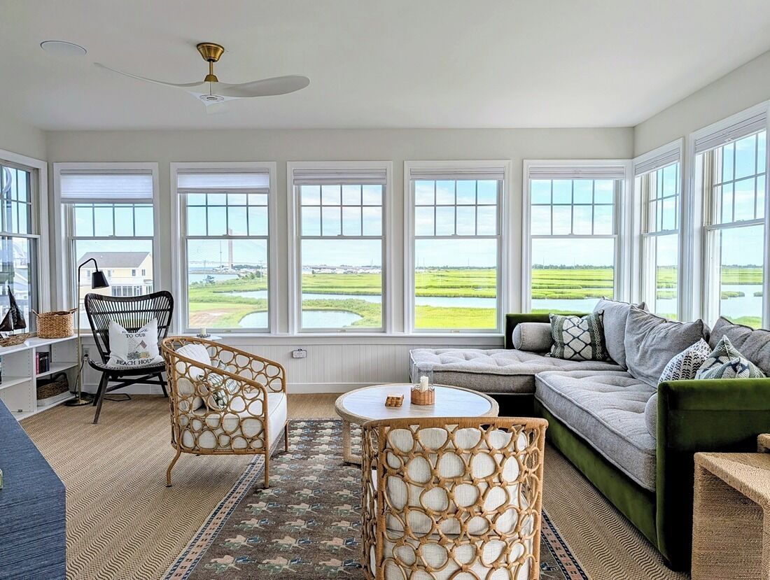 A spacious room with a large window, a green sofa, a wicker chair, and a small table.