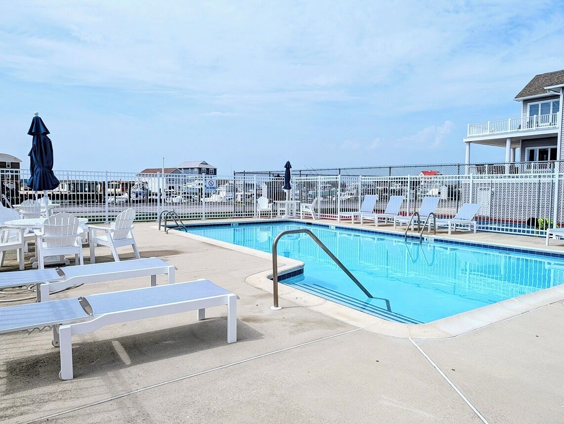 A swimming pool with lounge chairs and umbrellas, surrounded by a white fence.